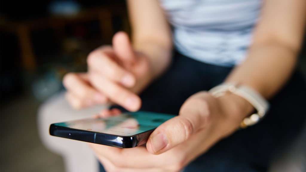 Close-up of a person using a smartphone, scrolling with their right hand. The person is wearing a watch on their left wrist.